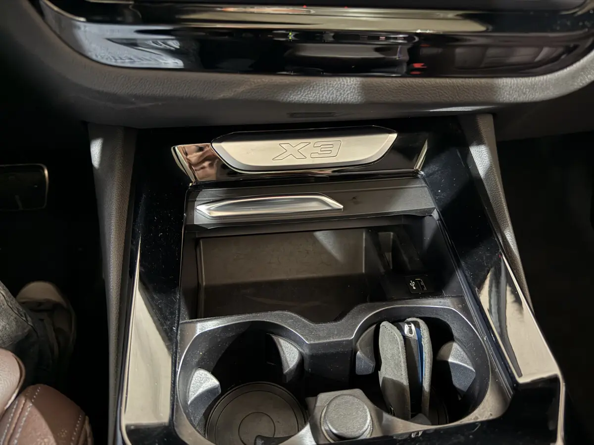 Gros plan sur la console centrale noire brillante du BMW X3 avec porte-gobelets et logo X3 en métal.