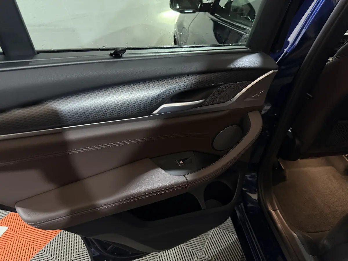 Vue intérieure du panneau de porte arrière droite bleu BMW X3 xDrive30e 2023 avec garniture cuir marron et commande de vitre électrique.