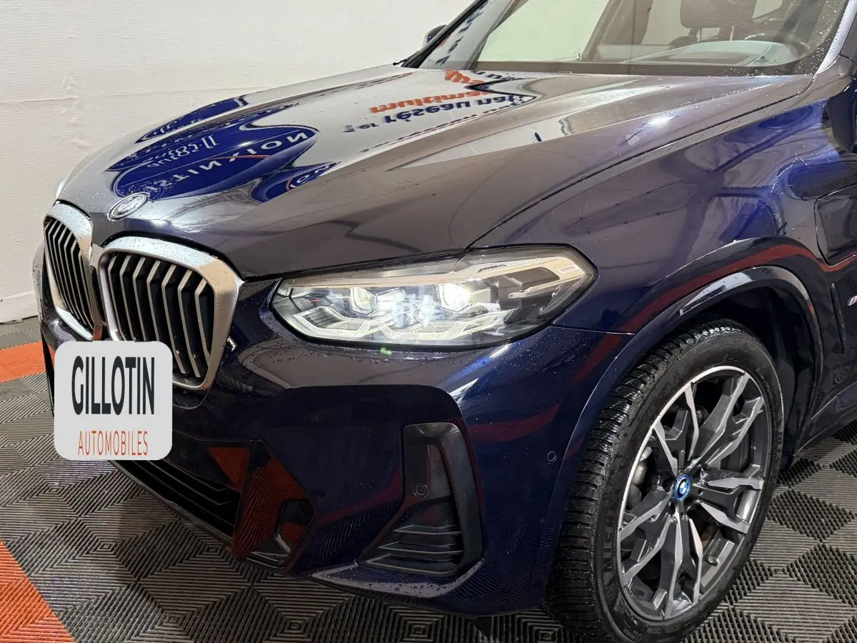 Vue 3/4 avant droit d’un BMW X3 xDrive30e bleu avec phares LED allumés et jantes alliage distinctives.