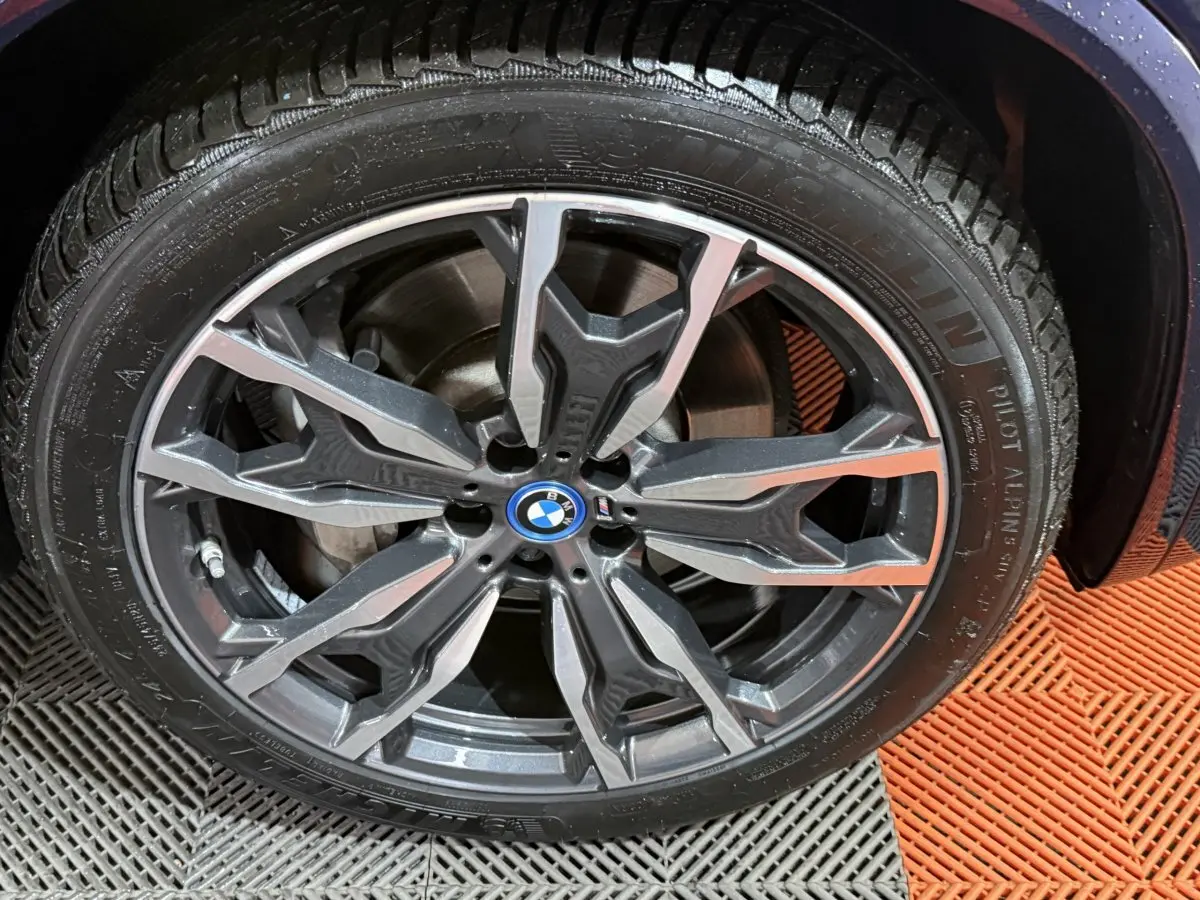 Gros plan sur la jante alliage grise et noire du BMW X3 xDrive30e bleu, avec logo BMW au centre.