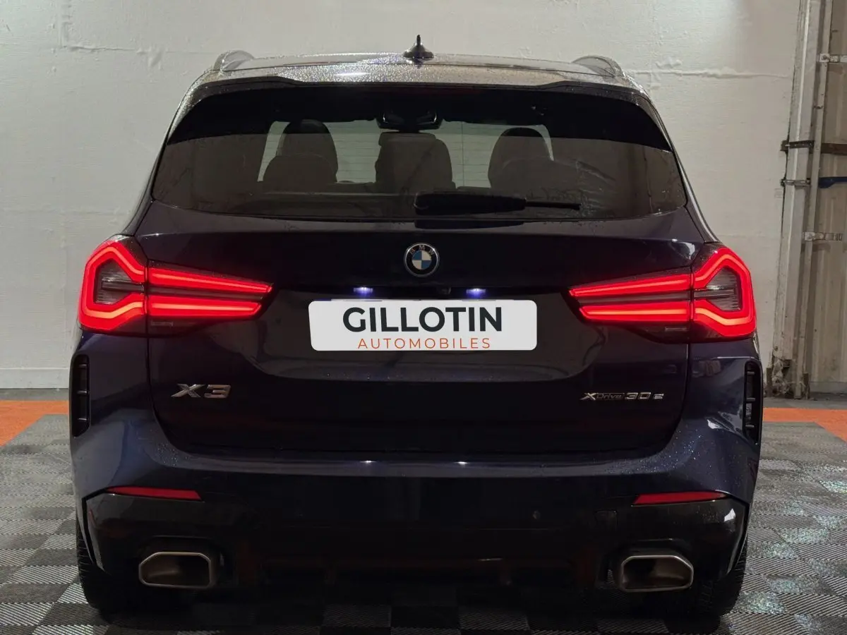 Vue arrière d’un BMW X3 xDrive30e bleu 2023 avec feux LED allumés et double sortie d’échappement rectangulaire.