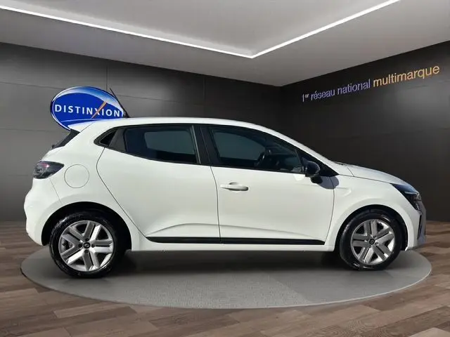 Vue latérale droite d'une Renault Clio V blanche avec enjoliveurs 16 pouces et vitres teintées, en intérieur showroom.