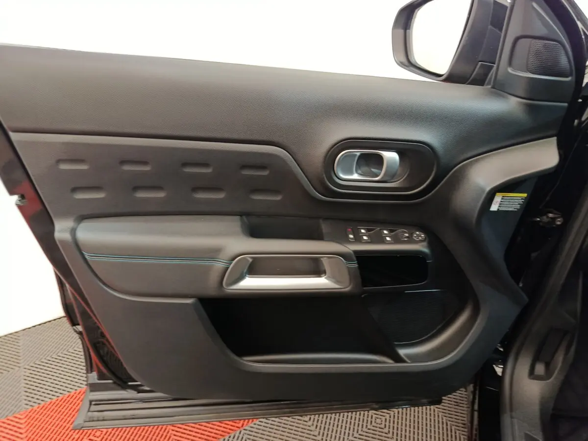 Vue intérieure côté gauche de la porte noire du Citroën C5 Aircross 2024 avec commandes de vitres et poignée argentée.