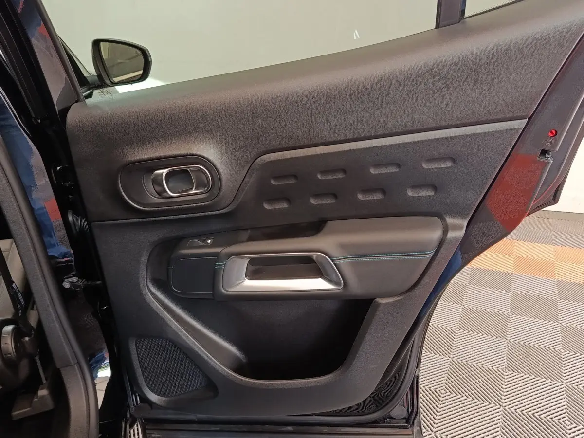 Vue intérieure de la porte arrière droite noire du Citroën C5 Aircross 2024 avec poignée argentée et surpiqûres bleues.