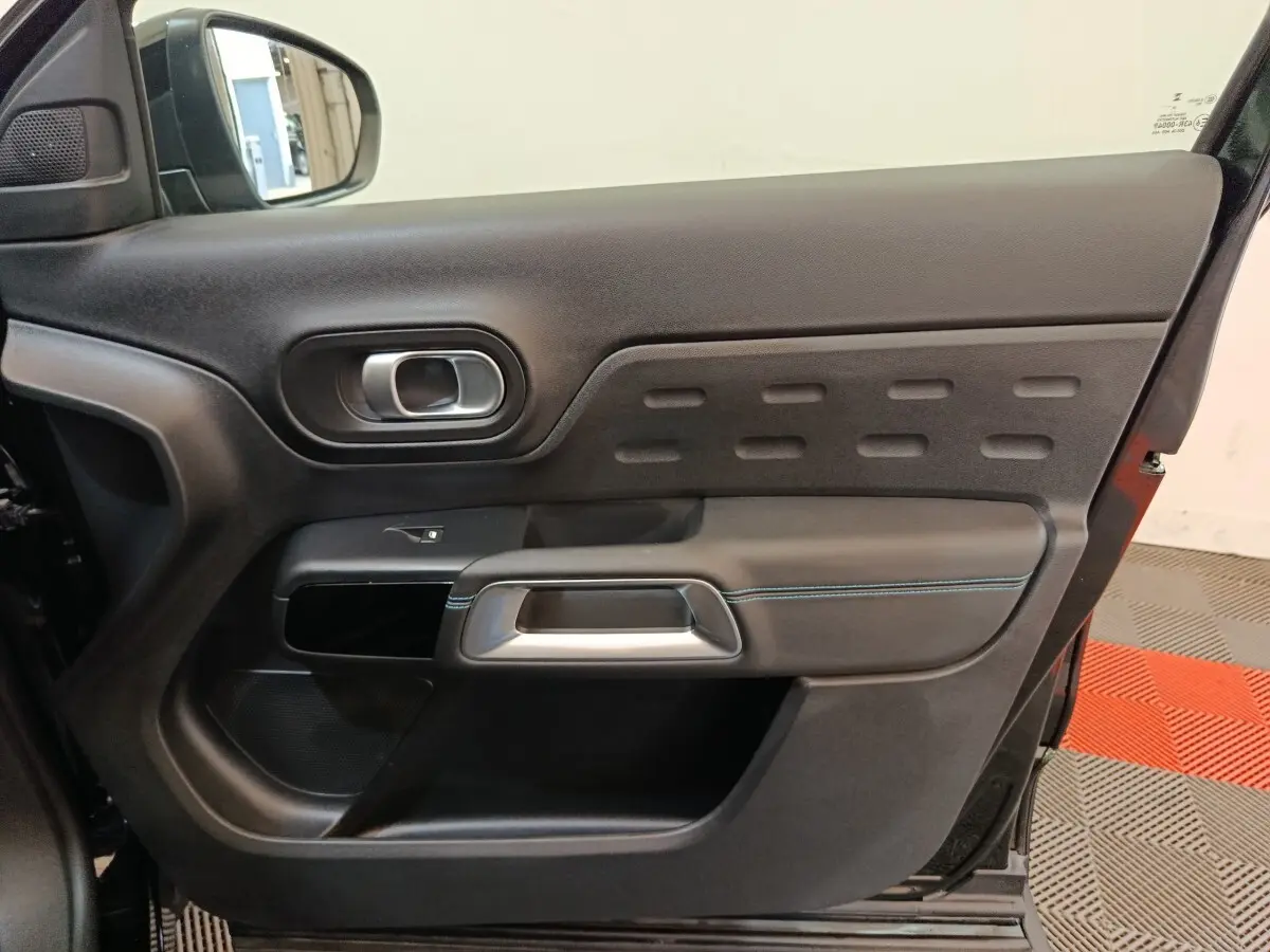 Vue intérieure de la porte arrière droite noire du Citroën C5 Aircross 2024 avec poignée argentée et surpiqûres bleues.