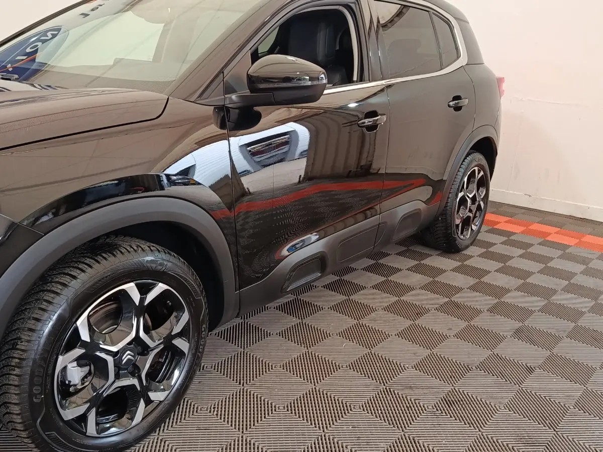 Vue côté gauche avant d'un Citroën C5 Aircross noir 2024 avec jantes noires brillantes et protections latérales.