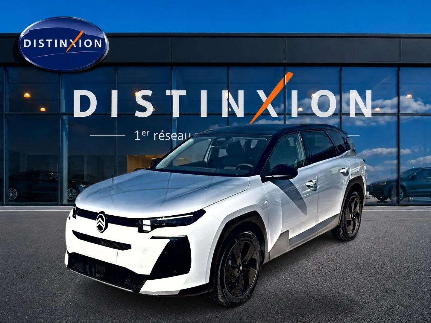 Vue 3/4 avant d'un Citroën C5 Aircross 2026 blanc avec toit noir et jantes alliage noires devant un showroom Distinxion.