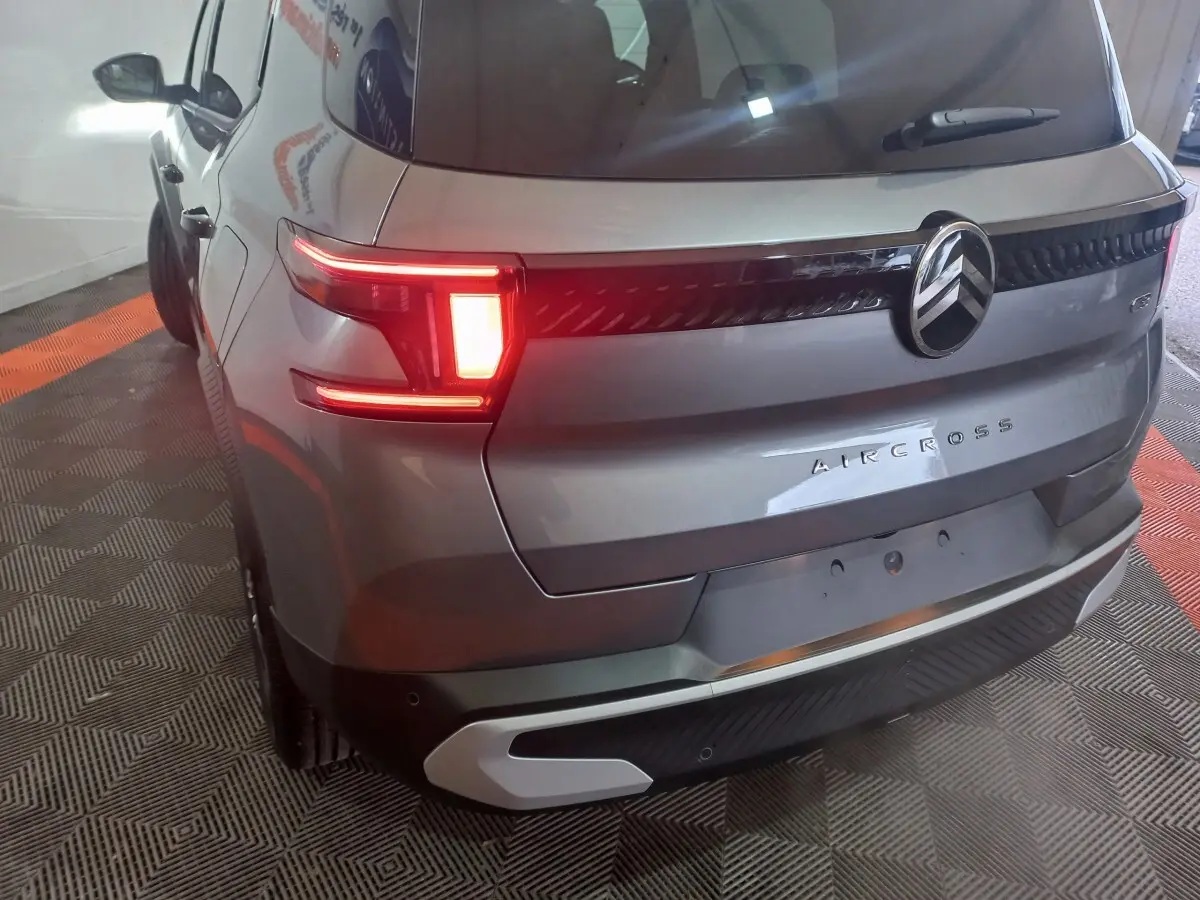Vue 3/4 arrière droite d'un Citroën Aircross gris foncé avec feux arrière allumés et logo central visible.