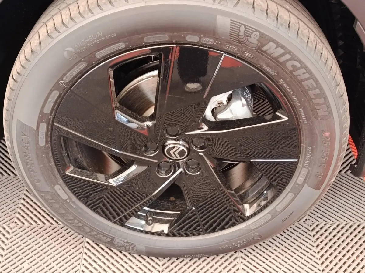 Gros plan sur la roue avant gauche noire brillante de la Citroën C5 Hybride 145ch auto MAX avec logo Citroën central.