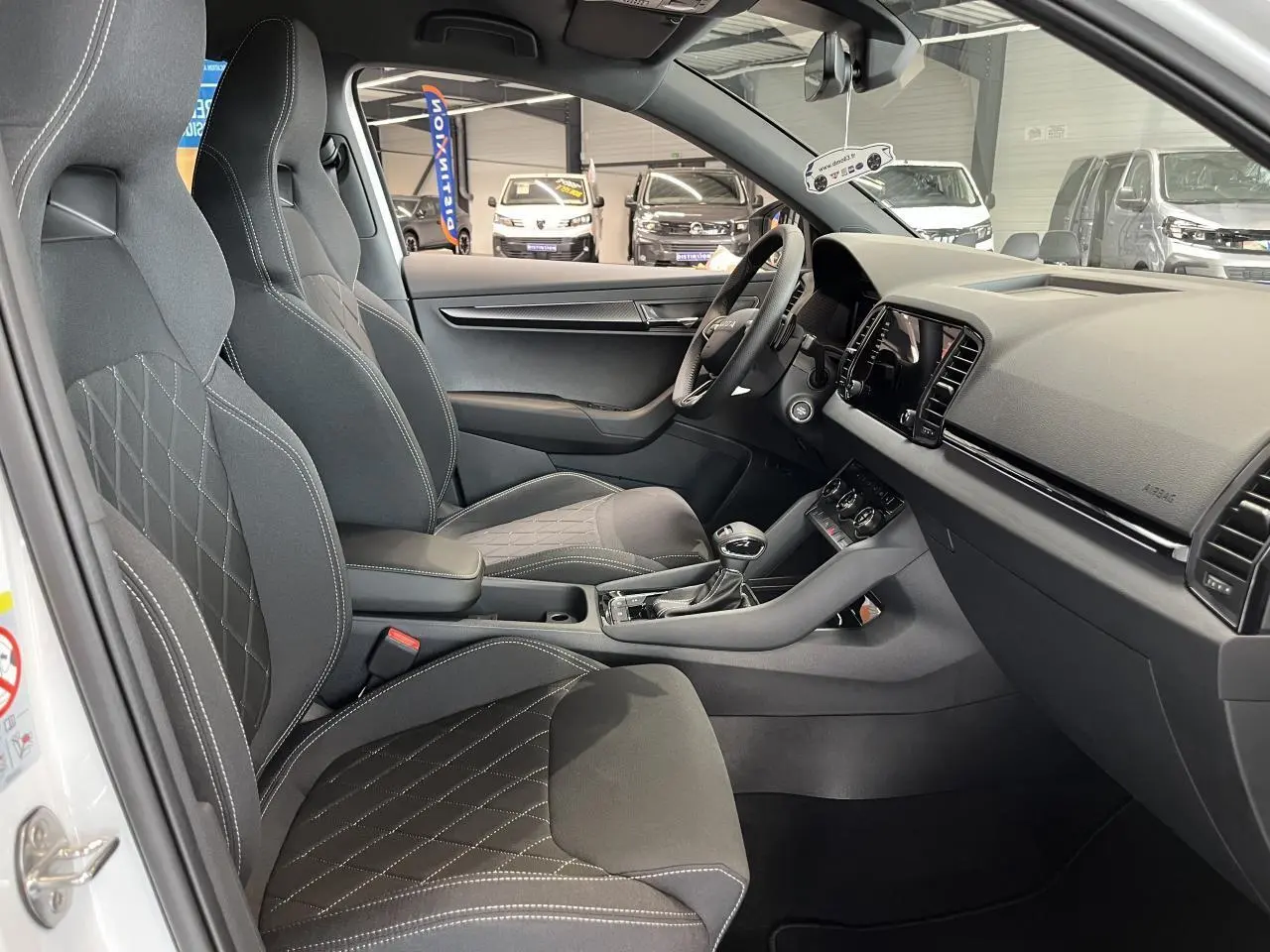 Intérieur avant droit d'un Skoda Karoq blanc 2025 avec sièges sport noirs et tableau de bord moderne.