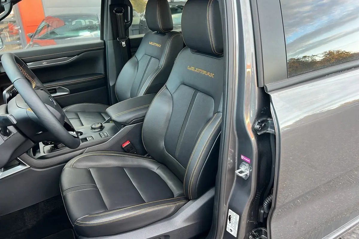 Vue intérieure côté conducteur du Ford Ranger 2025 gris carbone, sièges en cuir noir avec surpiqûres jaunes et logo Wildtrak brodé.