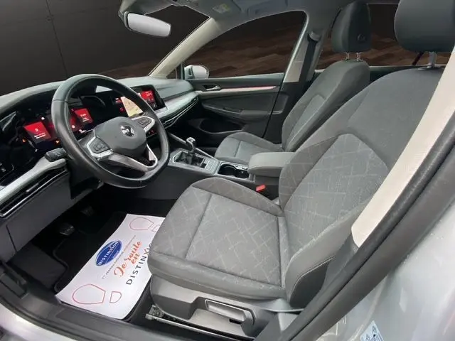 Vue intérieure côté conducteur de la Volkswagen Golf VIII gris argent, sièges tissu noir et tableau de bord moderne.