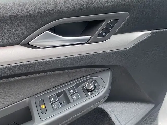 Détail de la porte côté conducteur de la Volkswagen Golf VIII gris argent, montrant les commandes des vitres et la poignée intérieure.