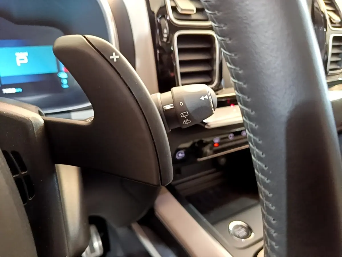 Gros plan sur la palette de changement de vitesse droite et le volant cuir du tableau de bord du Citroën C5 Aircross Hybrid blanc.