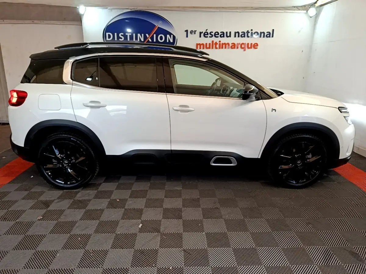 Profil droit d'un Citroën C5 Aircross blanc avec toit noir et jantes noires brillantes dans un showroom.
