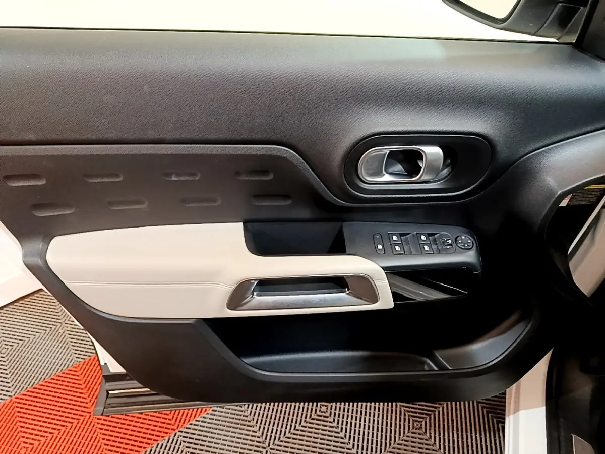 Vue intérieure sur la porte avant gauche du Citroën C5 Aircross blanc, avec garniture noire et beige et commandes électriques.
