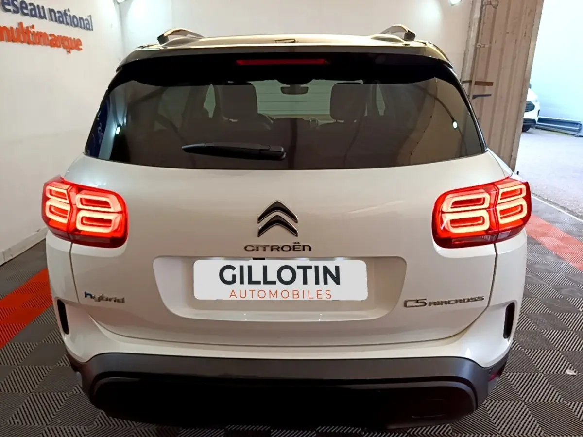 Vue arrière du Citroën C5 Aircross Hybrid blanc, feux arrière LED allumés et logo distinctif au centre du hayon.