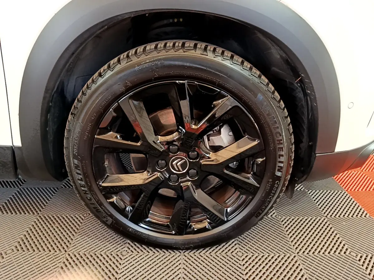 Gros plan sur la roue avant droite noire brillante d'un Citroën C5 Aircross blanc, avec logo Citroën au centre.