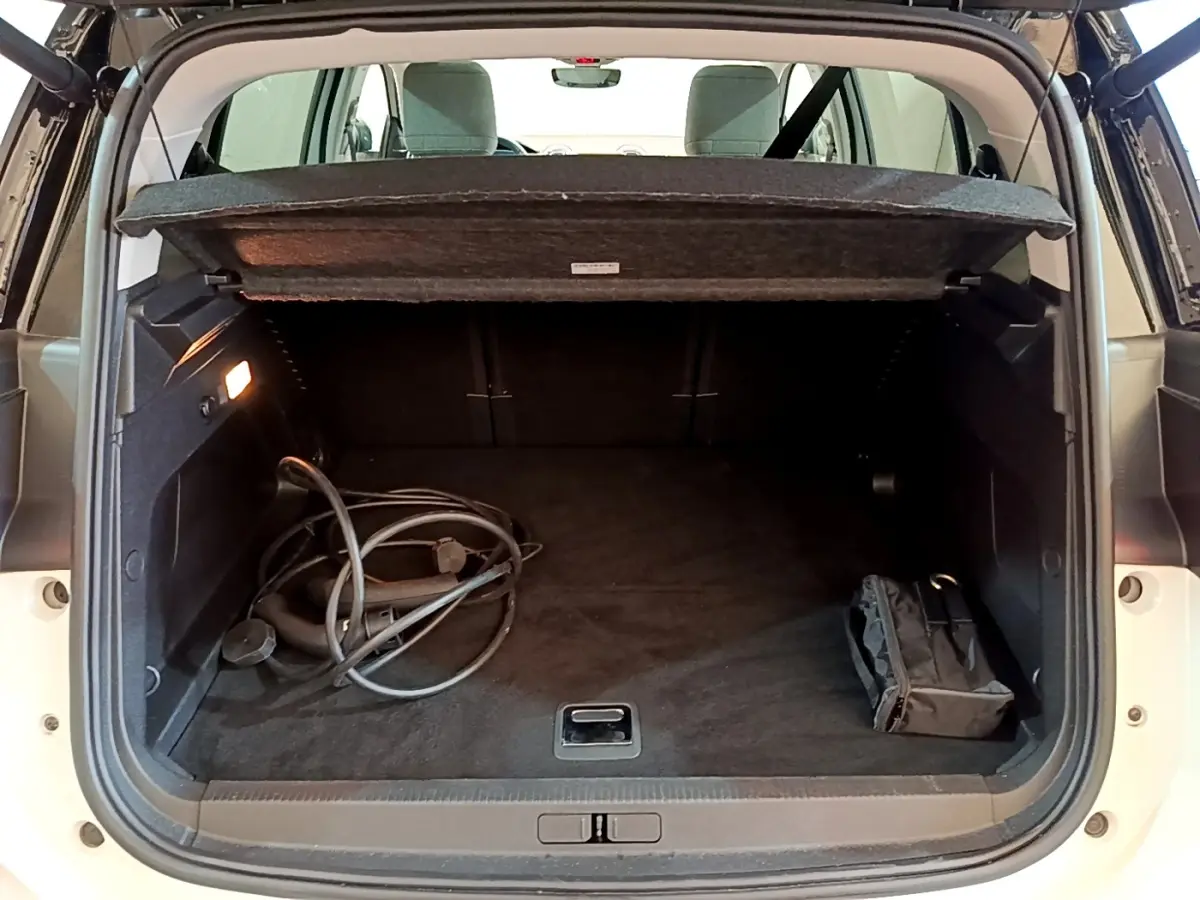 Vue arrière du coffre ouvert d'un Citroën C5 Aircross hybride blanc avec câble de recharge et sac noir à l'intérieur.