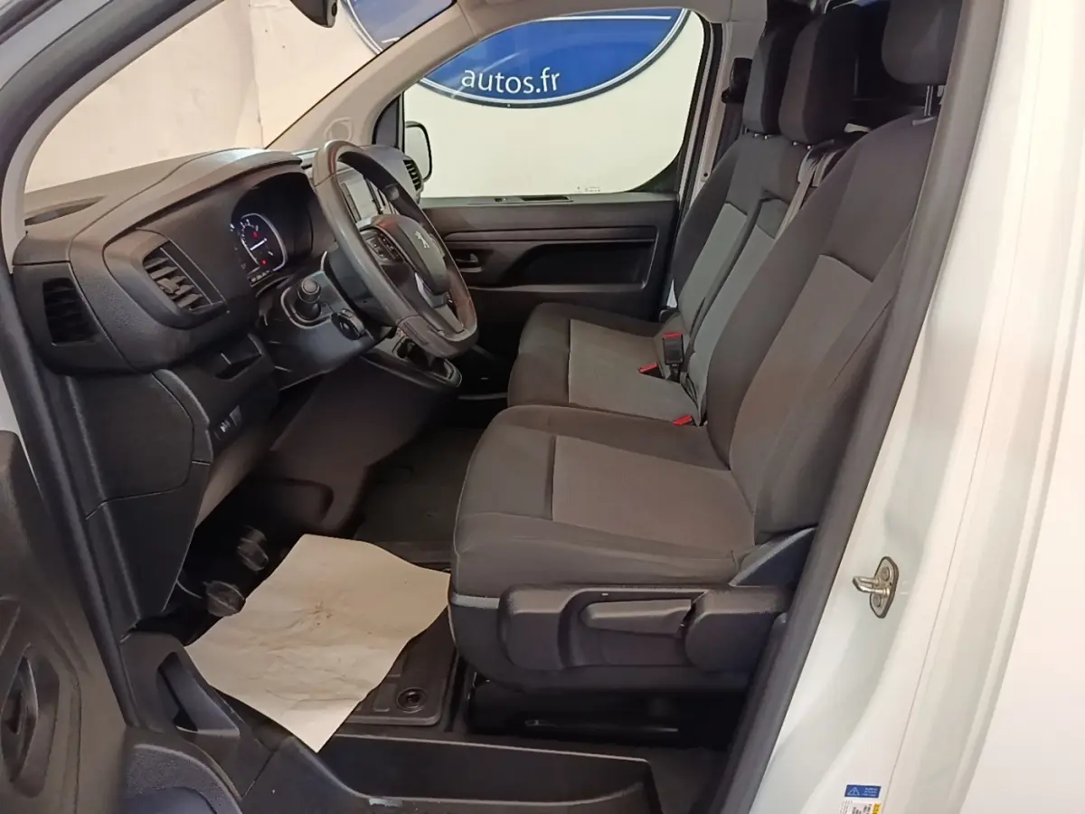 Vue intérieure côté conducteur du Peugeot Expert Fourgon blanc, montrant les sièges avant et le tableau de bord noir.