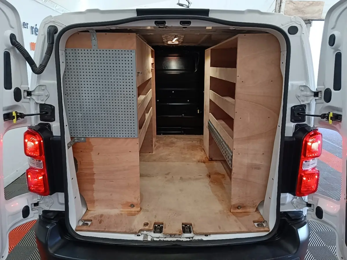 Vue arrière du Peugeot Expert Fourgon blanc 2023 avec portes ouvertes, montrant l’aménagement intérieur en bois pour rangement.