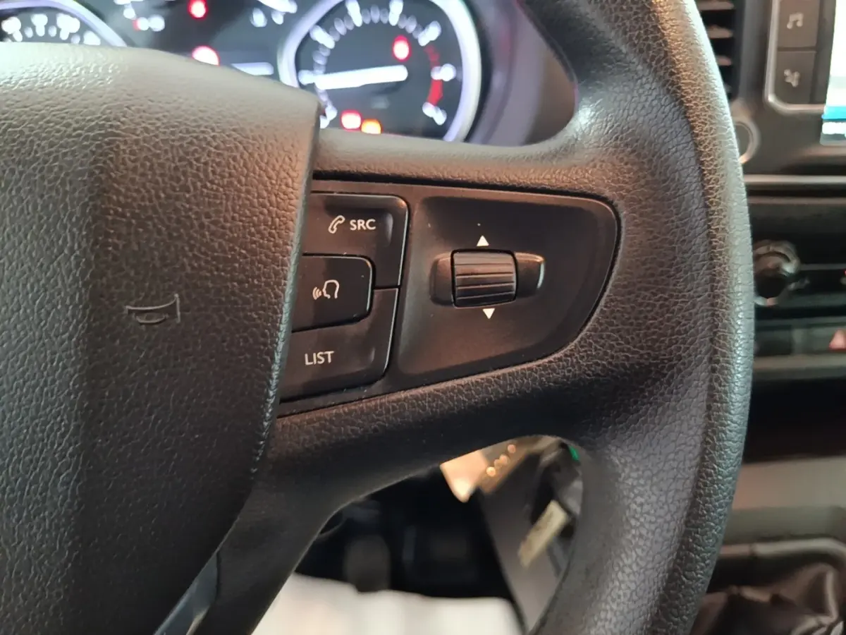 Gros plan sur le volant noir du Peugeot Expert Fourgon avec commandes audio et tableau de bord lumineux en arrière-plan.