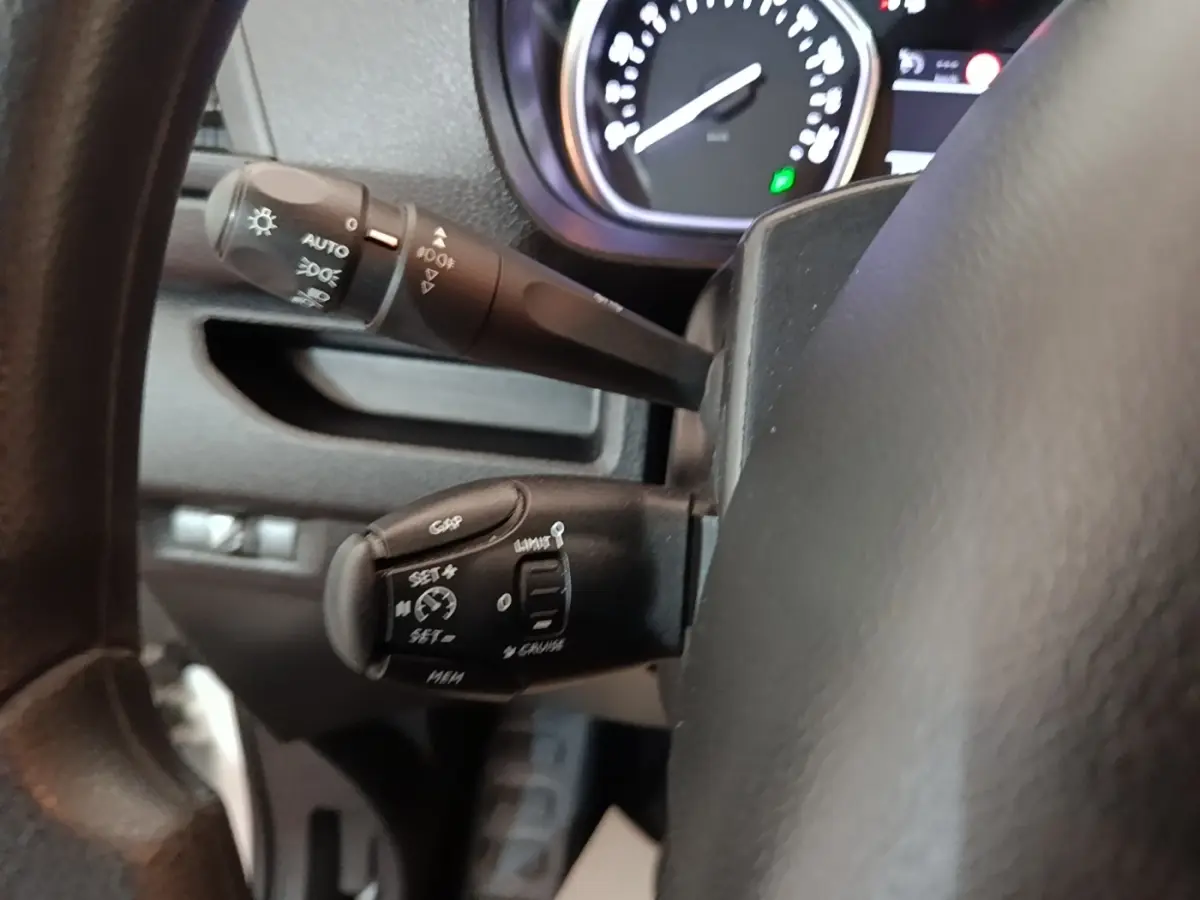 Gros plan sur les commandes du régulateur de vitesse et des feux derrière le volant noir du Peugeot Expert Fourgon blanc.