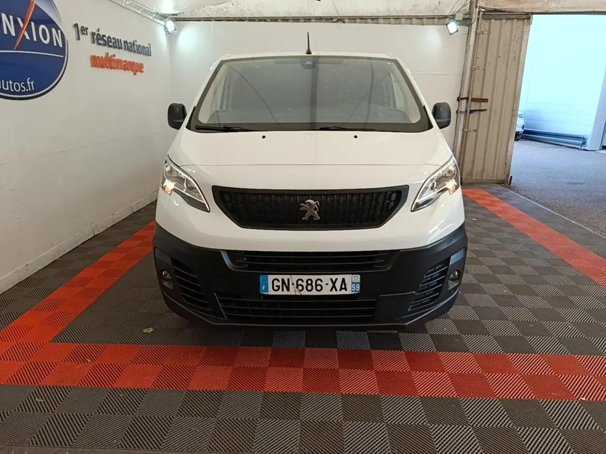 Vue frontale d’un Peugeot Expert Fourgon blanc 2023 avec calandre noire et pare-chocs avant noir dans un garage.