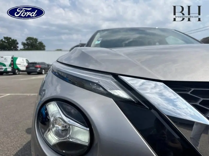 Gros plan sur le phare avant gauche du Nissan Juke gris perle métallisé, mettant en valeur son design moderne et ses lignes angulaires.