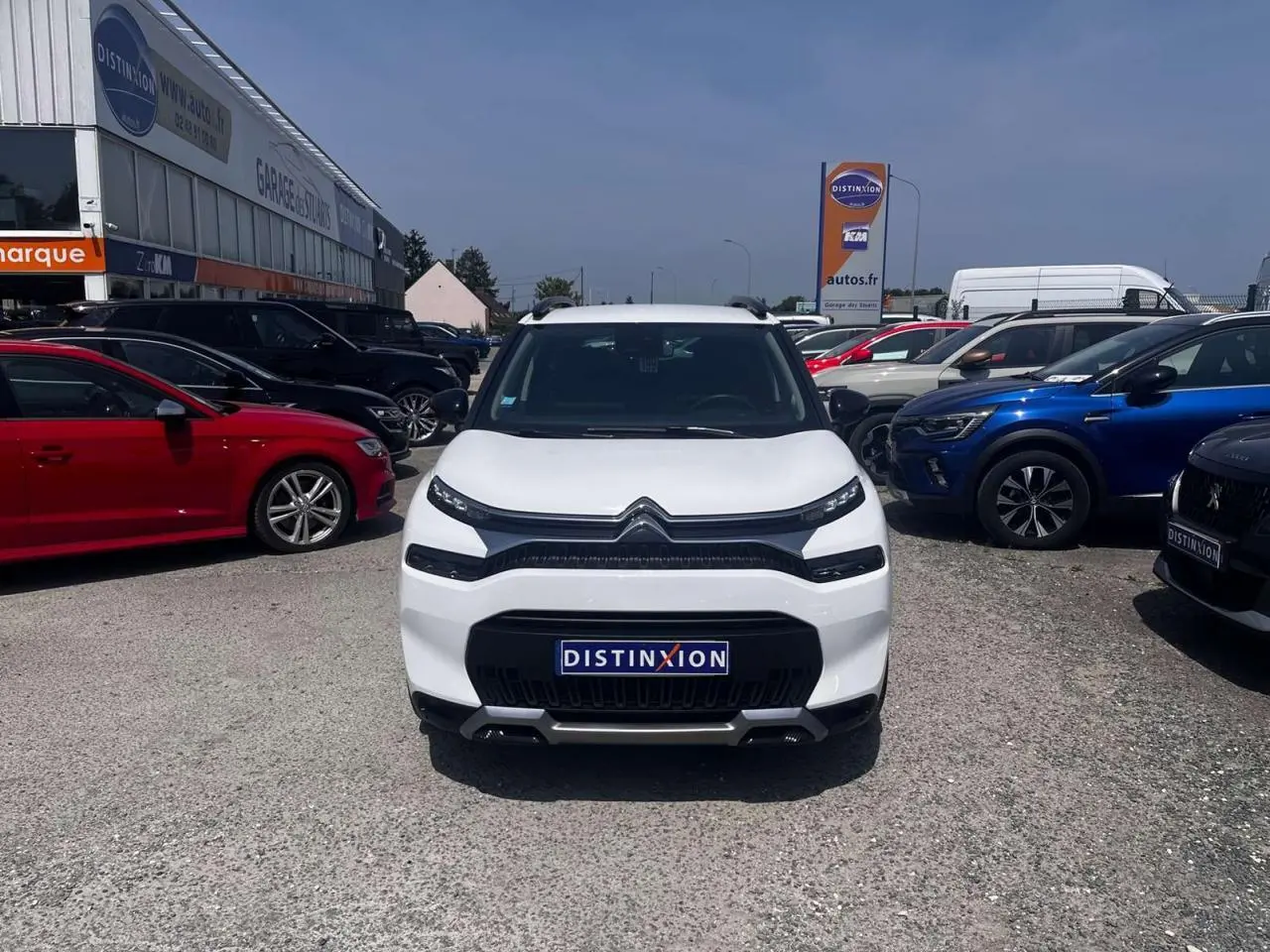 Vue avant d'un Citroën C3 Aircross blanc banquise avec calandre noire et barres de toit noires sur parking.