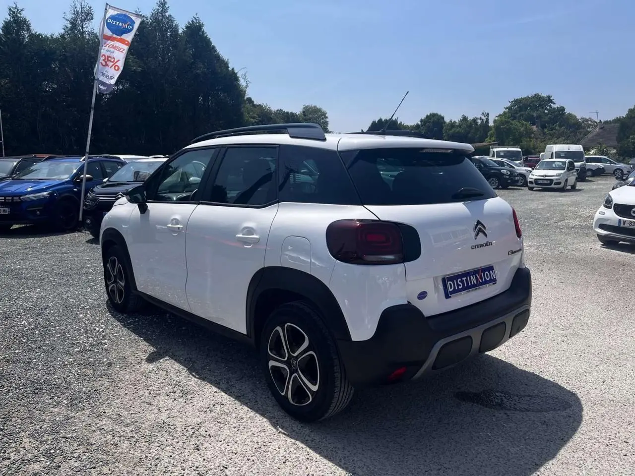 Vue 3/4 arrière droite d'un Citroën C3 Aircross blanc Banquise avec toit blanc et barres de toit noires.