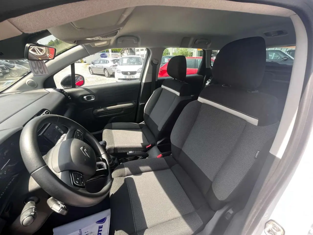 Vue intérieure côté conducteur du Citroën C3 Aircross blanc banquise, sièges tissu gris et volant multifonction.