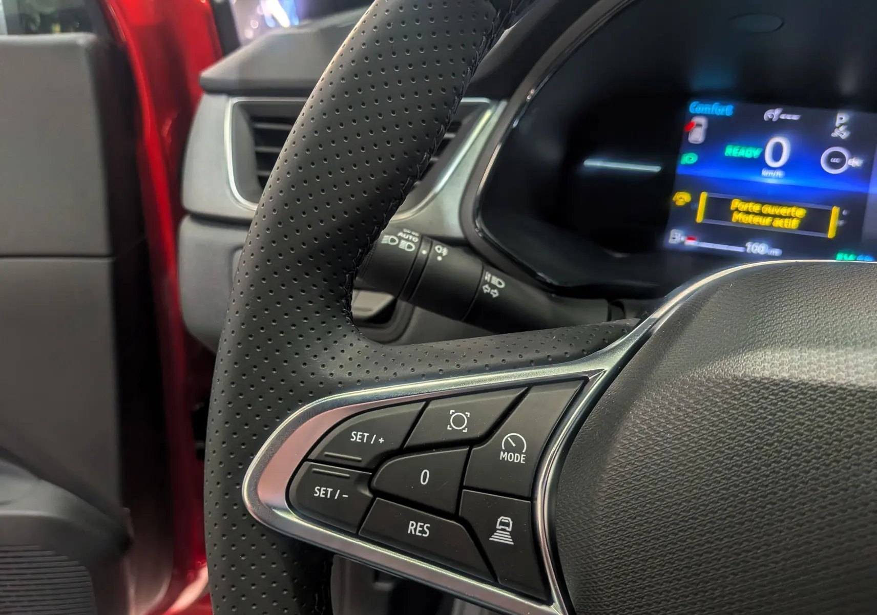 Gros plan sur le volant perforé du Renault Captur E-TECH 2025 rouge flamme, avec commandes intégrées et tableau de bord digital.