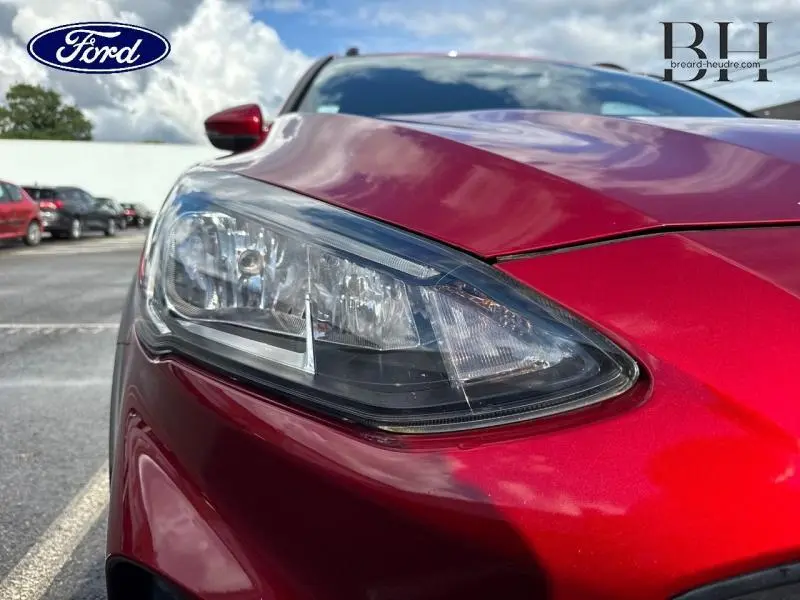 Gros plan sur le phare avant gauche d'une Ford Focus 1.0 EcoBoost 2020 en rouge Premium Candy, avec reflet du ciel.