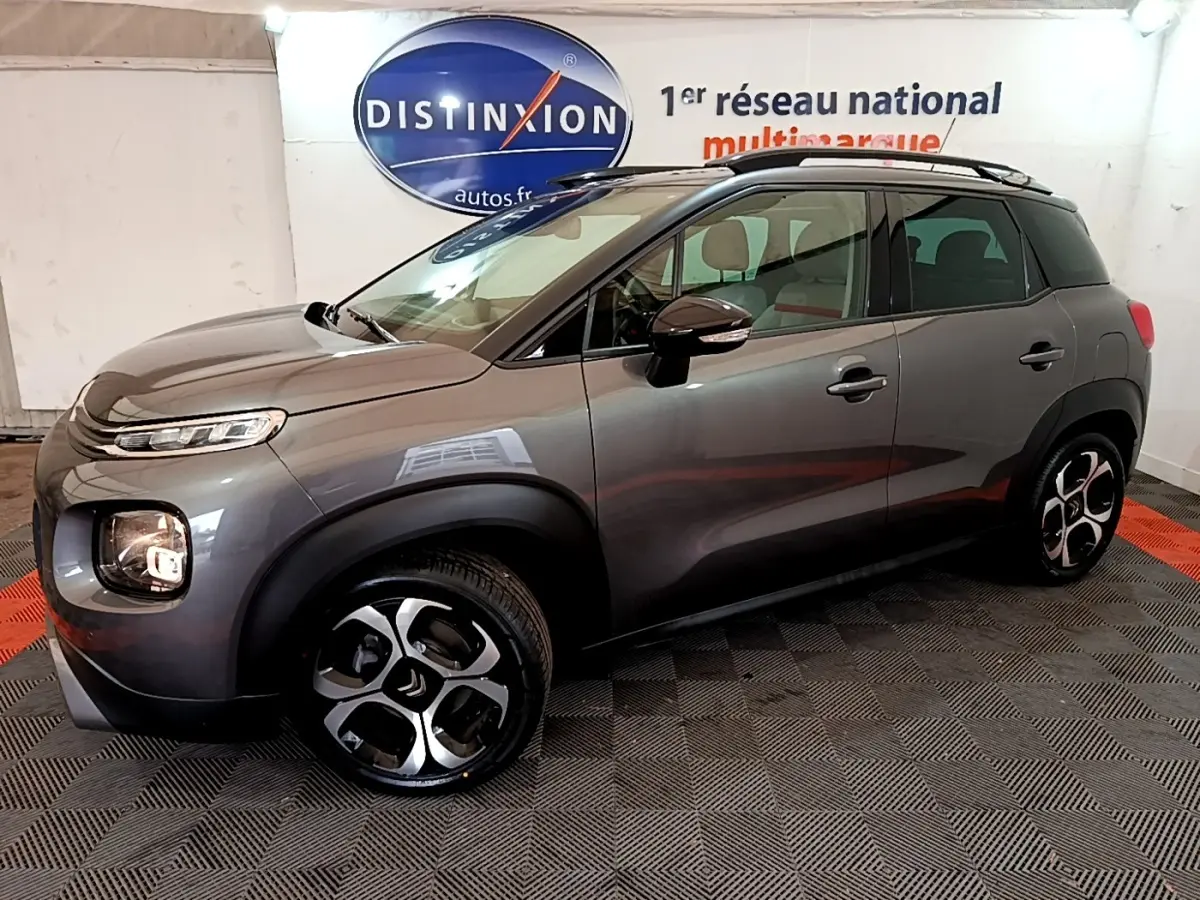 Vue 3/4 avant droit d'un Citroën C3 Aircross gris foncé avec jantes distinctives et barres de toit noires.