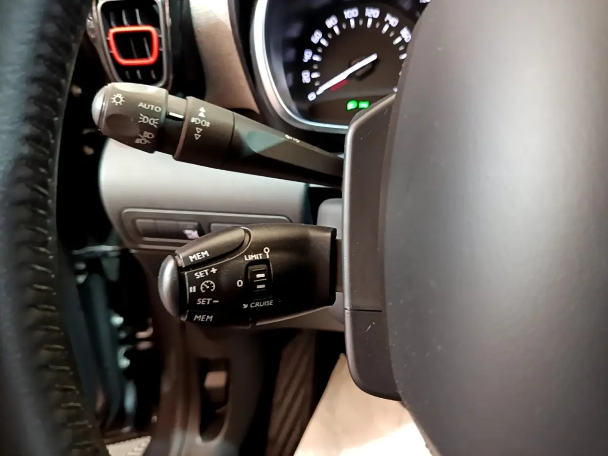 Gros plan sur les commandes au volant cuir du Citroën C3 Aircross gris foncé, avec tableau de bord partiellement visible.