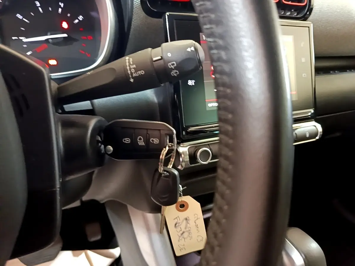 Gros plan intérieur sur le volant cuir et clé insérée du Citroën C3 Aircross gris foncé, avec tableau de bord et écran tactile visibles.
