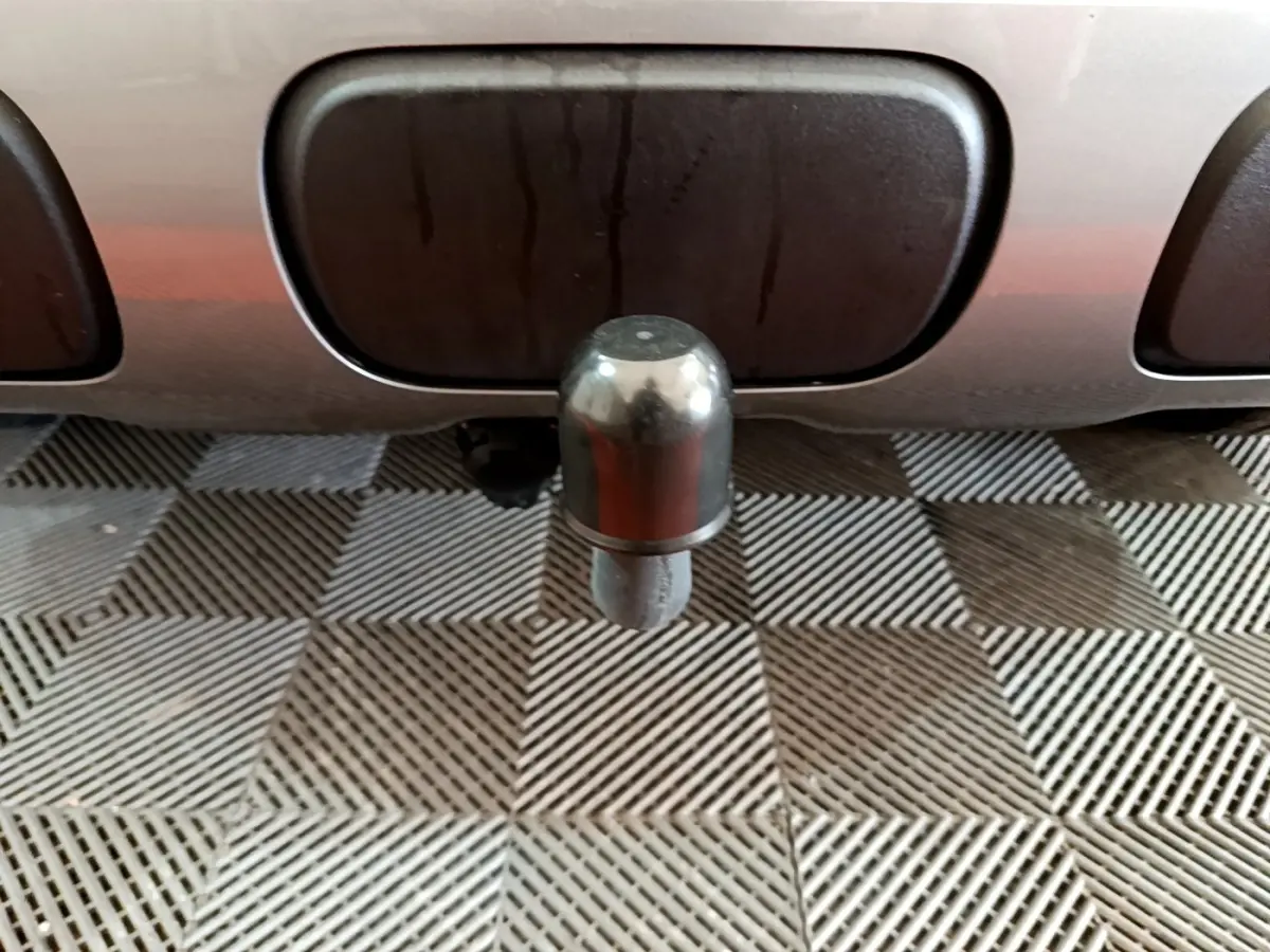 Gros plan sur l'attelage arrière métallique d'un Citroën C3 Aircross gris foncé, posé sur un sol à motifs géométriques.