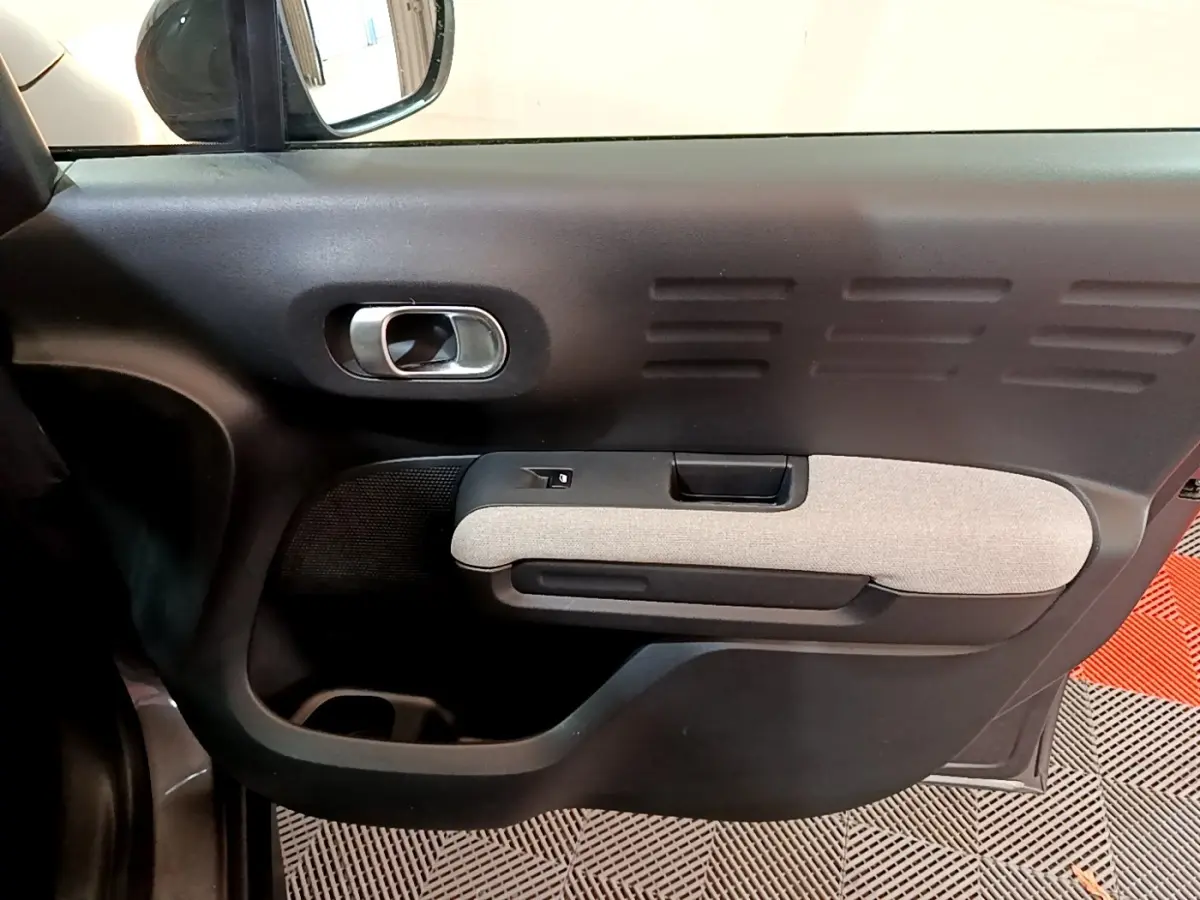 Vue intérieure côté gauche de la porte avant d'une Citroën C3 Aircross 2020 gris foncé avec accoudoir tissu clair.