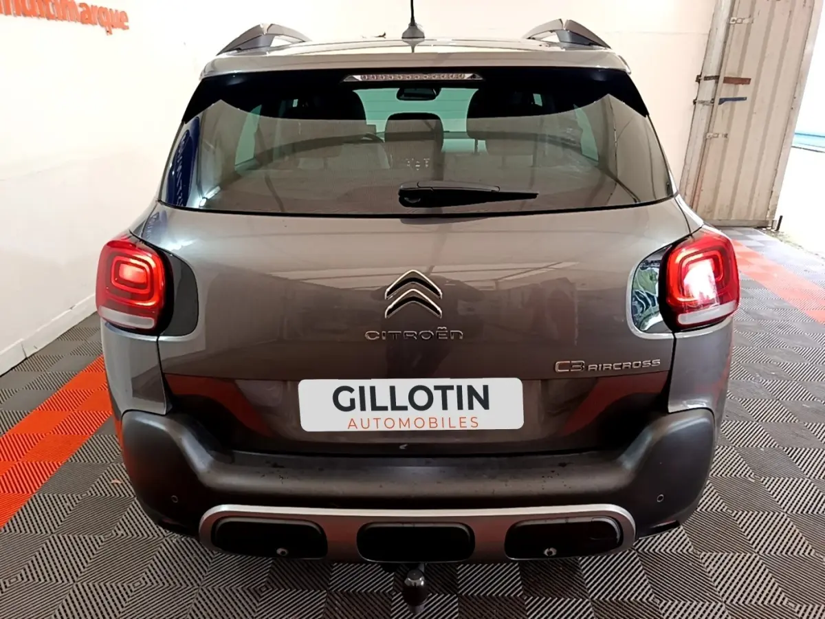 Vue arrière d'un Citroën C3 Aircross gris foncé avec feux arrière allumés et barres de toit visibles.