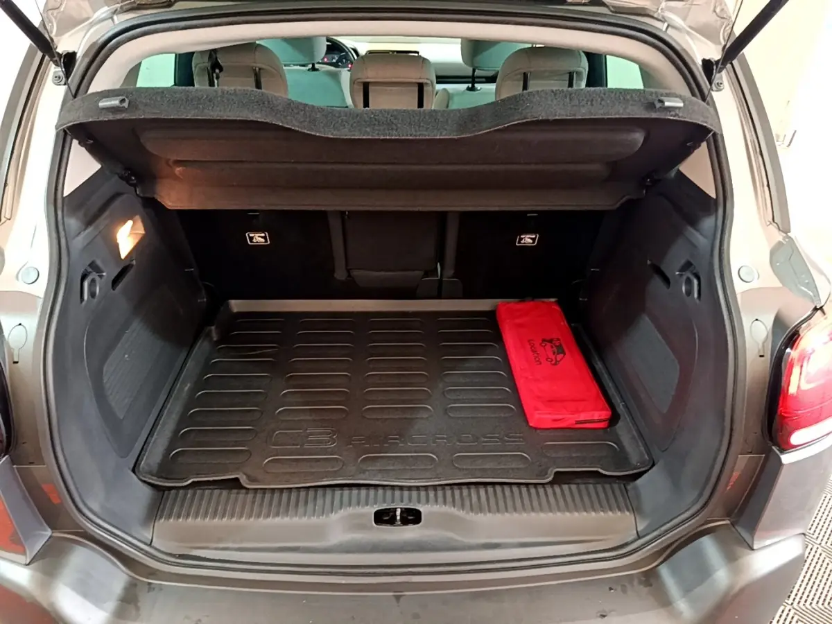 Coffre ouvert d’un Citroën C3 Aircross gris foncé, vue arrière avec tapis de coffre et trousse rouge visible.