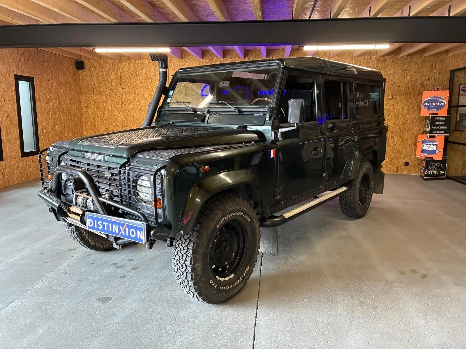 Land Rover Defender 110 vert vue 3/4 avant droit avec treuil, plaques de protection et pneus tout-terrain.