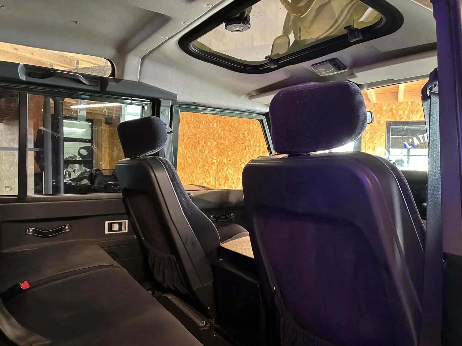 Intérieur arrière du Land Rover Defender 110 2005, vue côté gauche, sièges noirs et toit ouvrant visible.