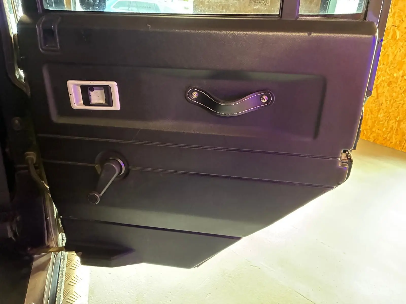 Vue rapprochée de la porte intérieure côté gauche du Land Rover Defender 110 2005, avec poignée et manivelle de vitre.