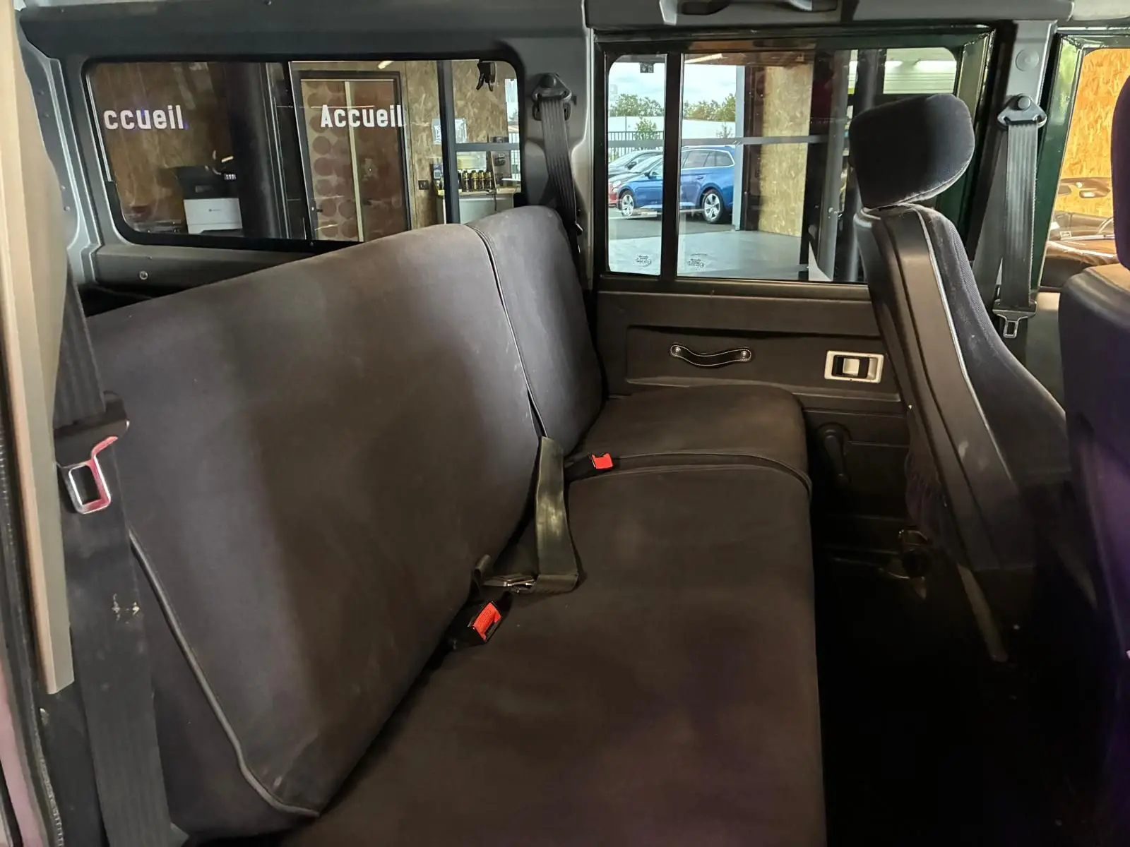 Vue intérieure côté gauche sur la banquette arrière noire du Land Rover Defender 110 vert de 2005.