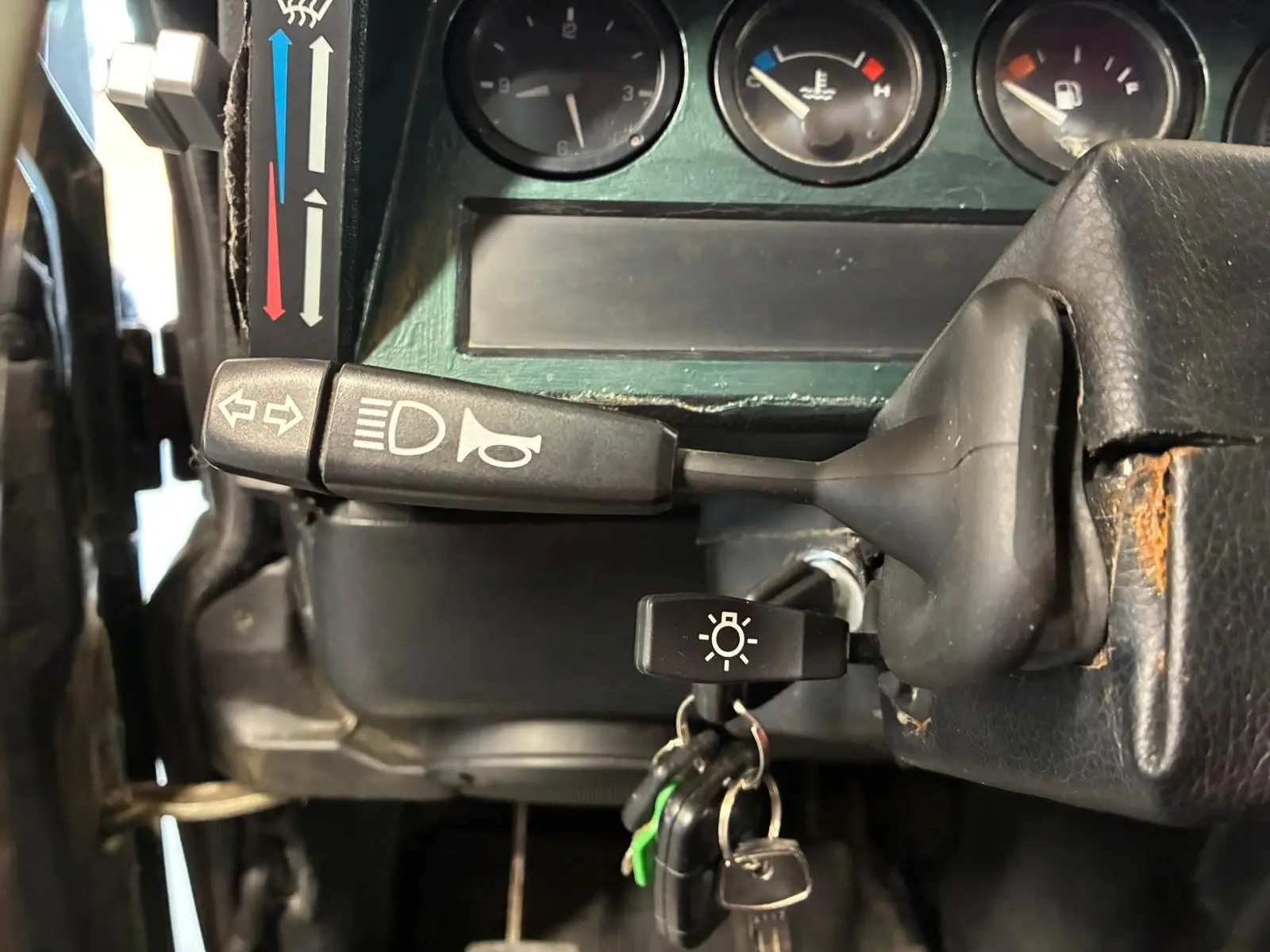 Détail du tableau de bord vert du Land Rover Defender 110 2005, avec manette de clignotants et clés sur le contacteur.