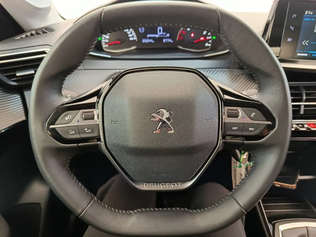 Vue rapprochée du volant cuir multifonctions noir d'une Peugeot 208 2022, avec tableau de bord digital en arrière-plan.