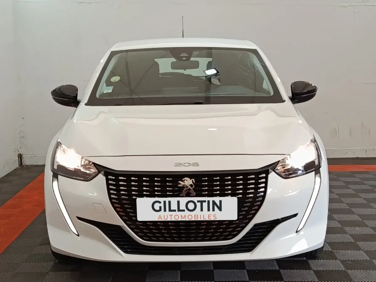 Vue avant d'une Peugeot 208 blanche avec feux allumés et calandre noire distinctive dans un showroom.