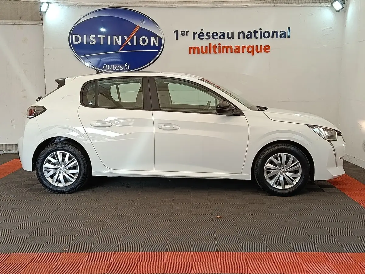 Profil côté gauche d'une Peugeot 208 blanche 2022 BlueHDi 100 S&S Active en intérieur, avec jantes alliage et rétroviseurs noirs.