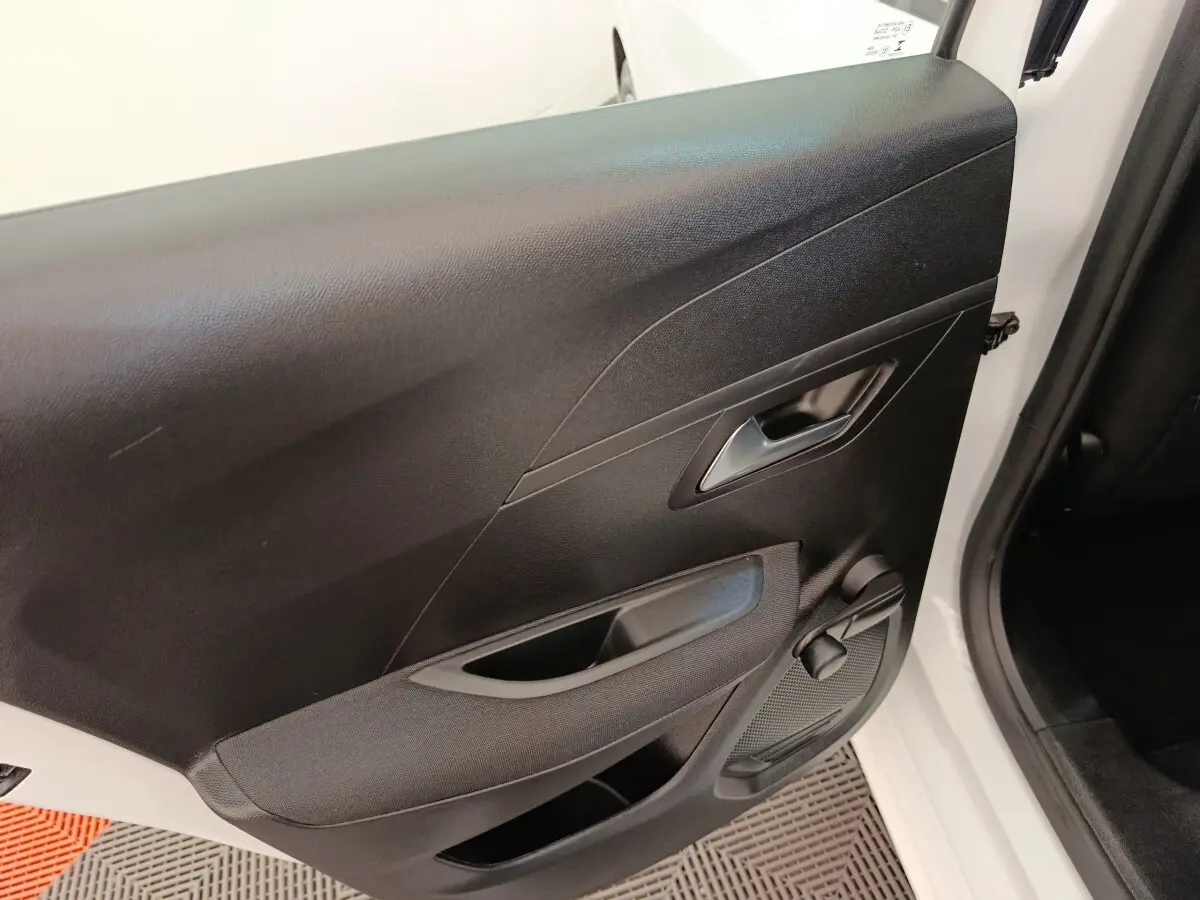 Vue rapprochée de la porte arrière droite noire avec poignée et manivelle de vitre d'une Peugeot 208 blanche.